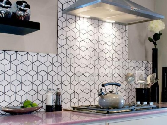 A sleek, neutral kitchen with a pink countertop, a black-and-white geometric tile backsplash, and stainless steel appliances