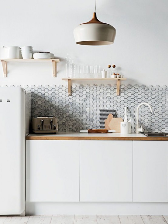 A Scandinavian kitchen in cream tones with sleek white cabinets, a white refrigerator, white countertops and a white marble hexagon tile backsplash