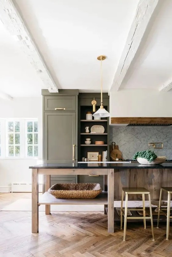 A beautiful farmhouse kitchen with an olive green cabinet and a stained kitchen island, a range hood, pendant lamps and gold and brass knobs
