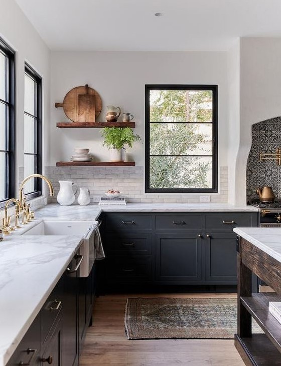 A chic dark gray farmhouse kitchen with white quartz countertops and a white marble tile backsplash, stained floating shelves and mixed metals