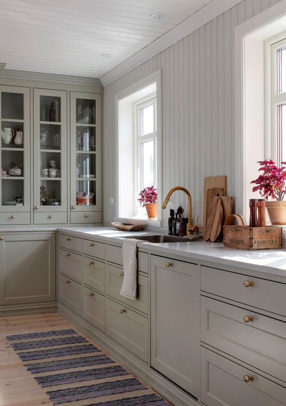 a chic kitchen with gray shaker cabinets and glass cabinets, a white beadboard backsplash, and a white stone countertop