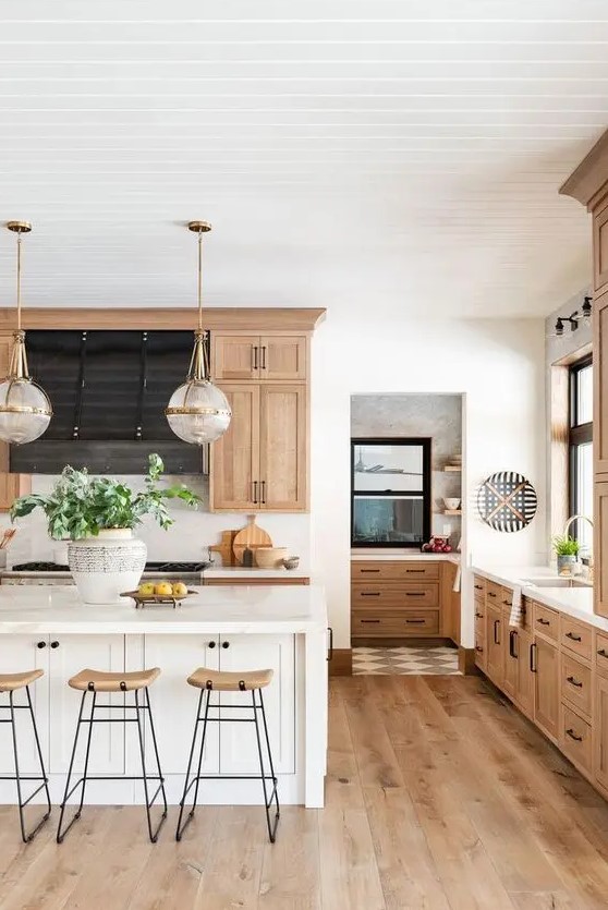a chic, modern farmhouse kitchen with light-stained cabinets and hardwood floors, a white island, high stools and pendant lamps
