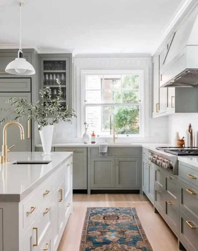 a classic sage green kitchen with shaker and glass front cabinets, a white stone and square tile countertop, a cream kitchen island