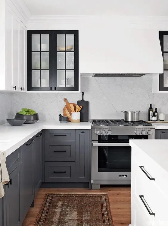 a contrasting kitchen with white upper cabinets and charcoal gray cabinets, black glass framed cabinets and a white backsplash and worktop