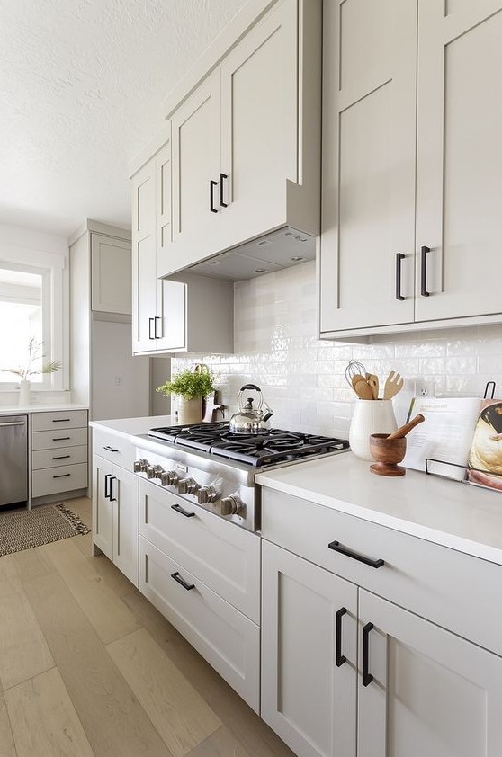 a gray farmhouse kitchen with shaker-style cabinets, a white tile backsplash and white countertops, and black fixtures