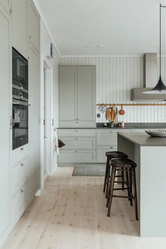 a light gray modern farmhouse kitchen with shaker style cabinets, black countertops and built-in appliances, a modern extractor hood and high stools