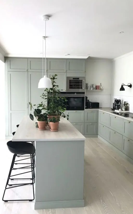 A beautiful pale green modern farmhouse kitchen with neutral countertops and tall black stools and sconces is a chic space