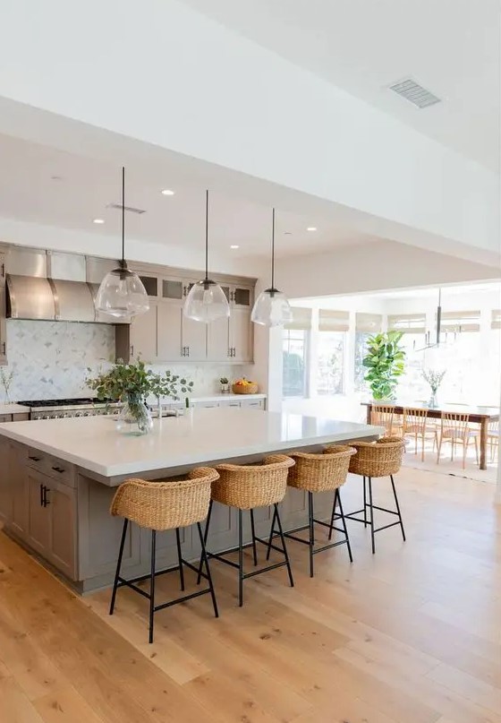 A modern farmhouse kitchen in dove gray with shaker-style cabinets, a large island, a pendant lamp and wicker stools