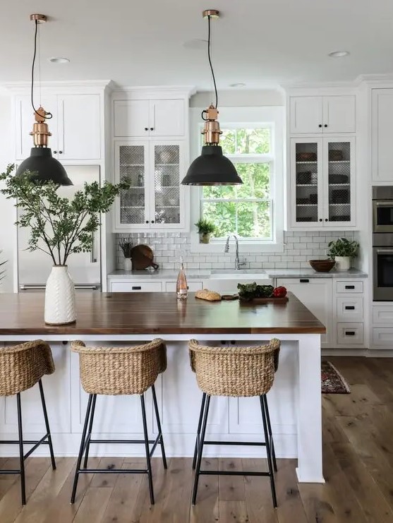 a modern white farmhouse kitchen with cool cabinets, a large kitchen island with butcher block countertops, pendant lamps and wicker stools