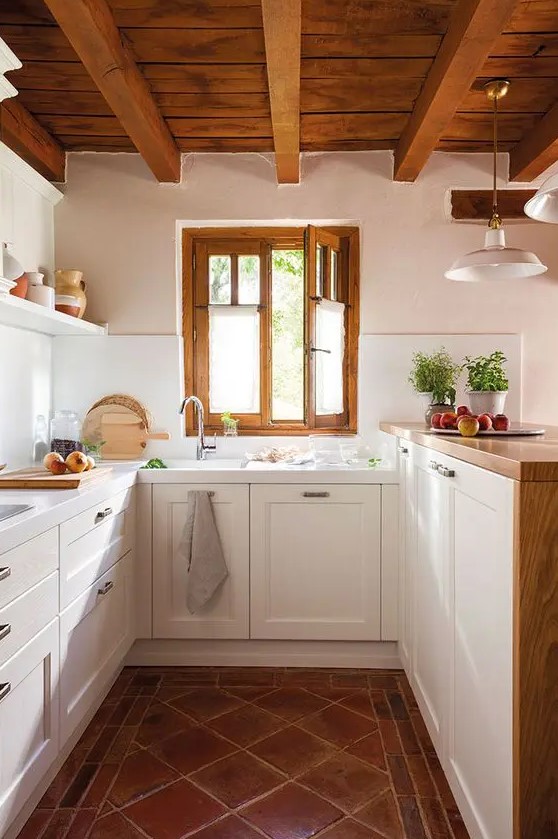 a modern country kitchen with tiled floors, white cabinets and raised butcher block countertops, a wooden ceiling with beams and frames on the window
