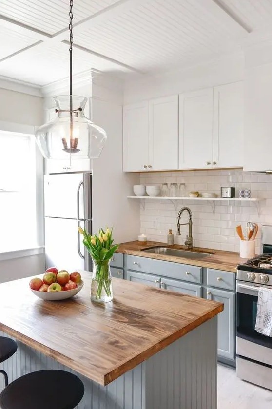 a modern farmhouse kitchen with white and light gray cabinets, butcher block countertops, a glossy subway tile backsplash, and a pendant lamp