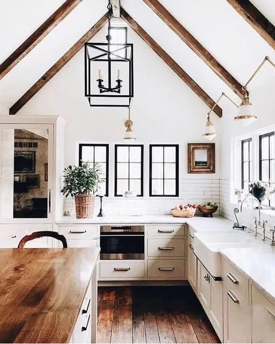 a modern dove gray country kitchen with dark wooden beams on the ceiling, pendant lamps and a kitchen island with a butcher block countertop
