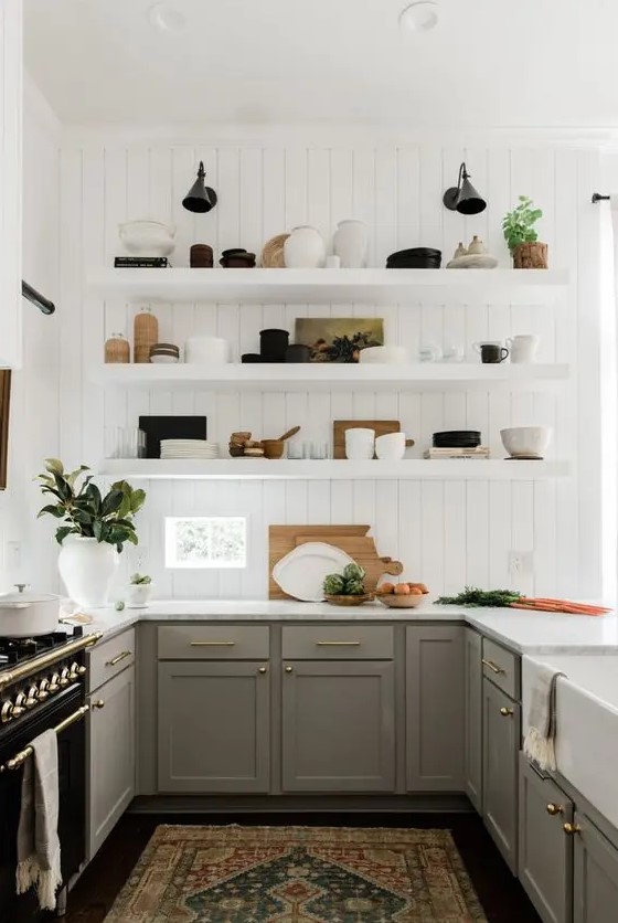A modern English country kitchen with white planked walls, gray Shaker-style cabinets, open shelving, gold accents and potted plants