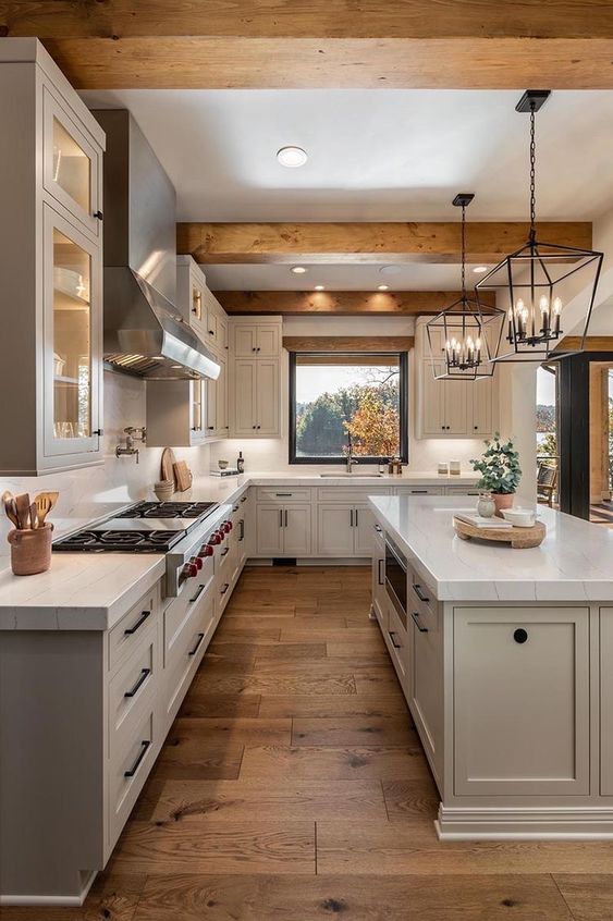 A modern dove gray farmhouse kitchen with stone countertops, wooden beams on the ceiling and statement pendant lamps