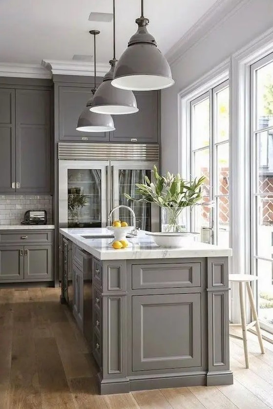 A modern gray farmhouse kitchen with shaker-style cabinets, a white subway tile backsplash, white marble countertops, and gray pendant lamps
