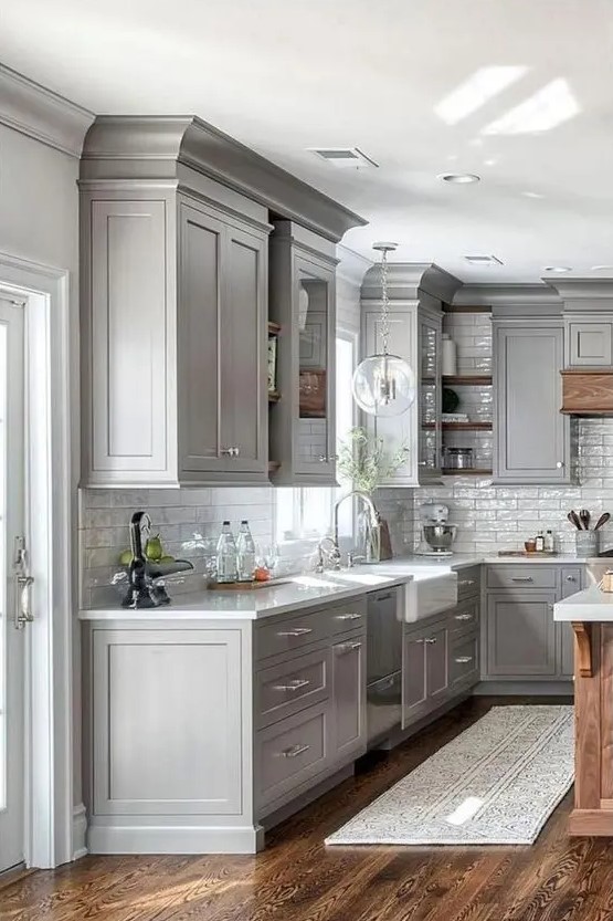 A modern gray farmhouse kitchen with white stone countertops and a white subway tile backsplash with neutral fixtures is chic