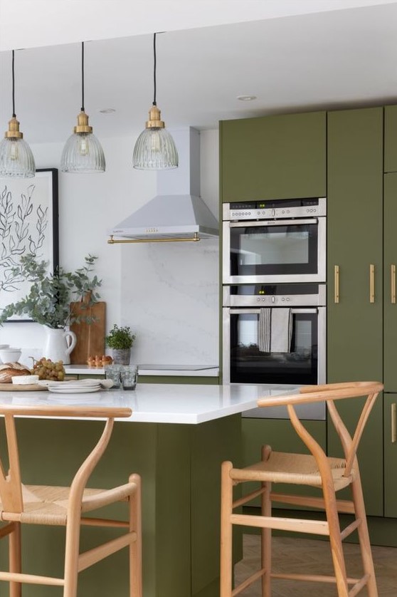 a modern farmhouse kitchen in olive green with elegant cabinets, a matching kitchen island, wishbone chairs and pendant lamps