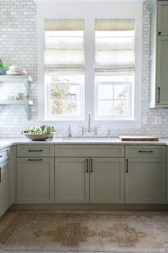 A modern sage green farmhouse kitchen with shaker cabinets, white stone countertops, white marble tiles and vintage fixtures