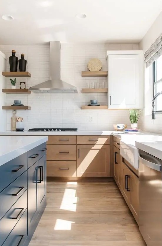 a modern farmhouse kitchen with light stained cabinets, a navy island, white stone countertops and a narrow tile backsplash and black handles