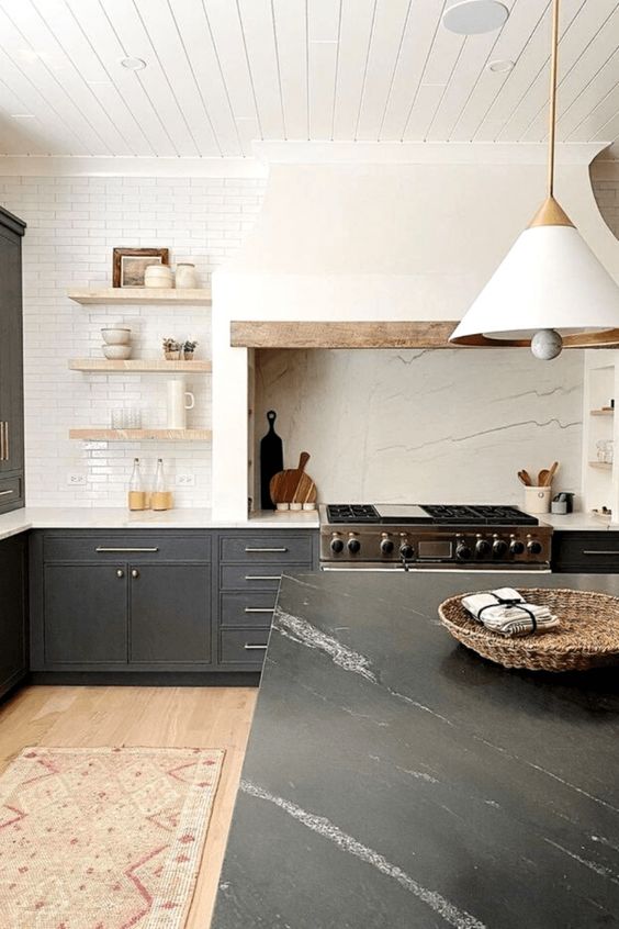 a modern farmhouse kitchen with soot cabinets, a large white extractor hood, open shelving and a kitchen island with stone countertops