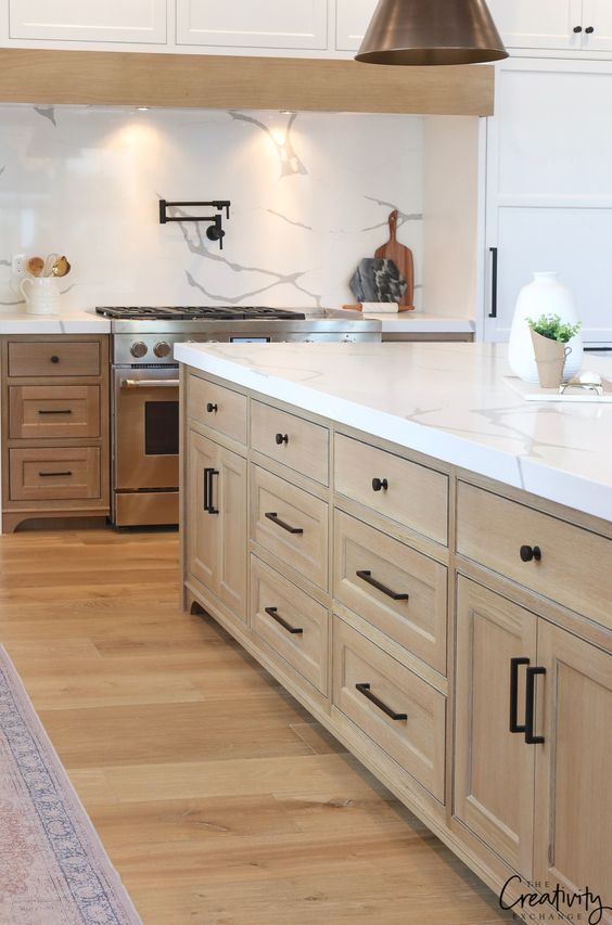 a modern farmhouse kitchen with stained and white cabinets, white stone countertops and backsplash, and pendant lamps