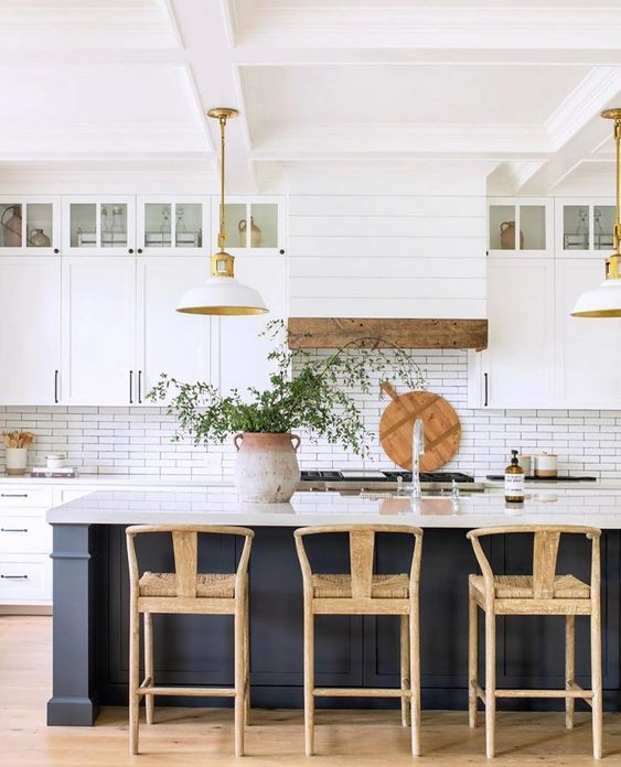 a modern farmhouse kitchen with white cabinets, a soot kitchen island, pendant lamps, woven stools and wood accents