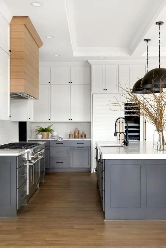 A modern farmhouse kitchen with white upper cabinets, dark gray lower cabinets, white countertops and backsplash, and black pendant lamps