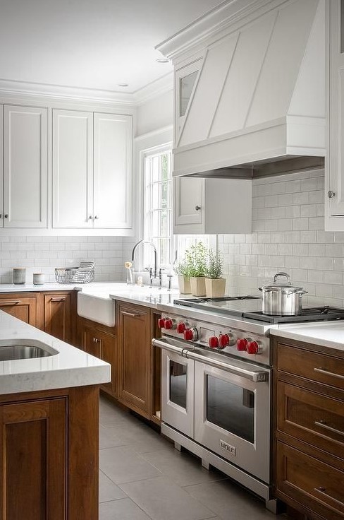 A modern two-tone kitchen with white upper cabinets and stained lower cabinets, white stone countertops and a white painted metal hood is great