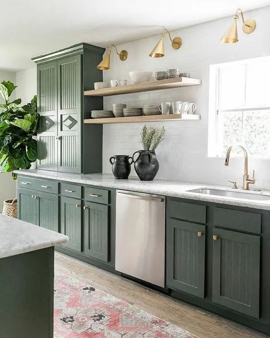 A stylish olive green farmhouse kitchen with fluted cabinets, white stone countertops, open shelving, and brass and gold lamps