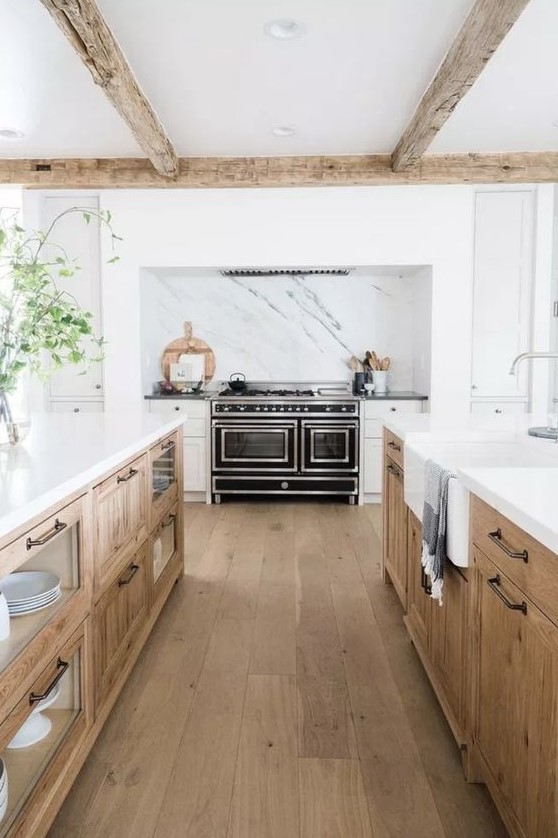 an inviting modern farmhouse kitchen with white and stained cabinets, white stone countertops, exposed beams and a black stove