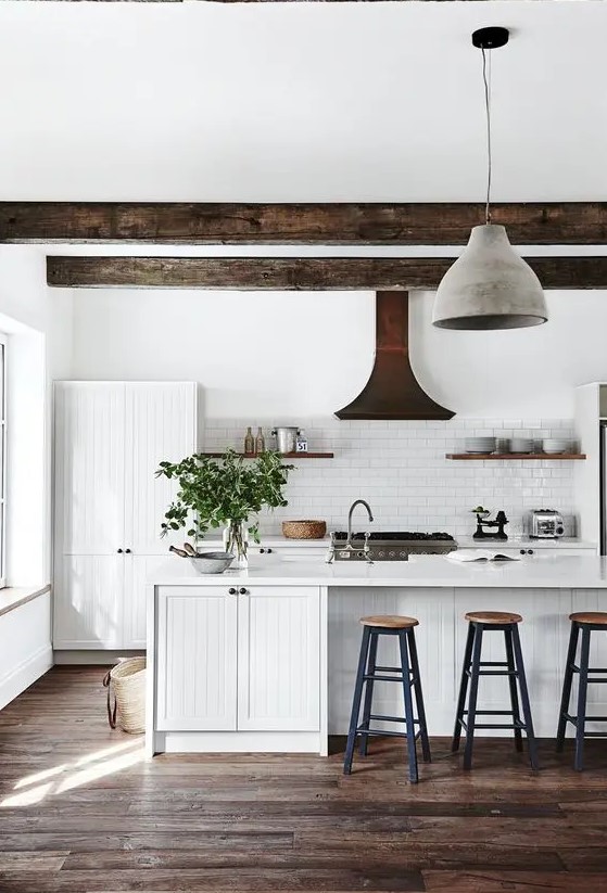 a white, modern country house kitchen with white planked cabinets, dark ceiling beams, pendant lamps, high stools and shelves