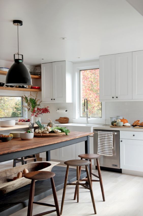 a white, modern farmhouse kitchen with shaker cabinets, a soot table and island, pendant lamps and wooden stools