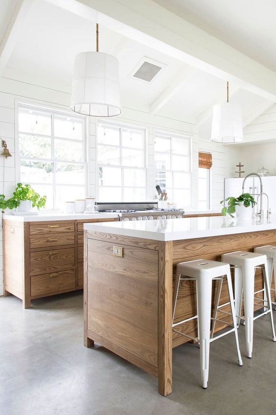 an airy, modern farmhouse kitchen with stained cabinets and an island, white stone countertops and hanging lamps
