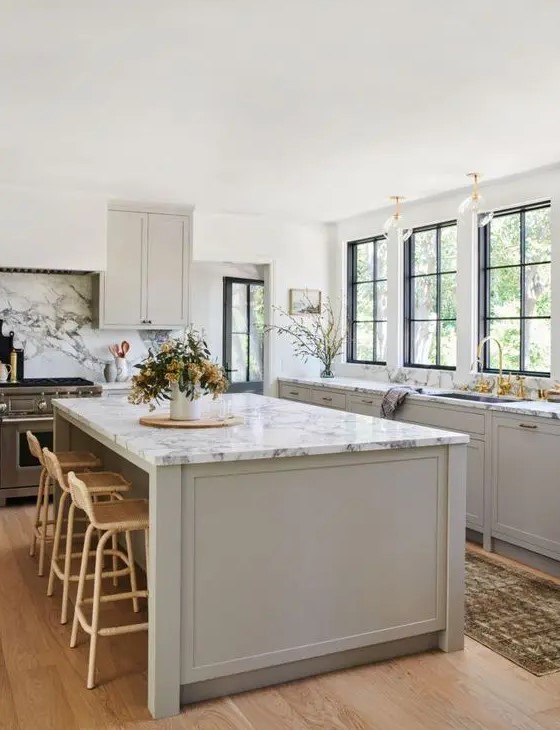 An inspiring dove gray modern farmhouse kitchen with shaker-style cabinets, white marble countertops, gold accents and rattan stools