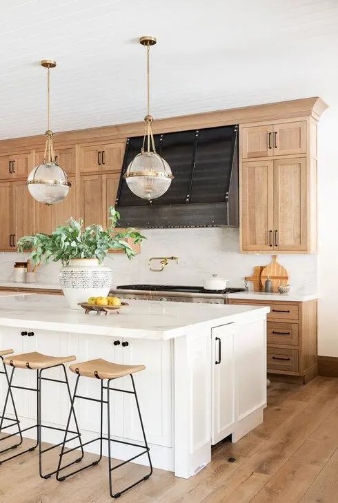 An inviting farmhouse kitchen features light-stained Shaker-style cabinets, white stone countertops and a white backsplash, wooden stools and a white kitchen island