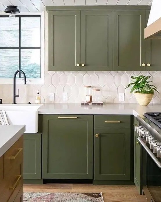 an olive farmhouse kitchen with shaker cabinets, a striking white tile backsplash, black fixtures, and gold handles and knobs