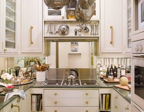 an elegant small kitchen with white cabinets, gold hardware, a mirrored backsplash and dark countertops