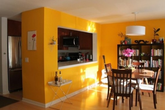 a small kitchen in a bright yellow cube with a window between the dining area and a bar cart and shelf