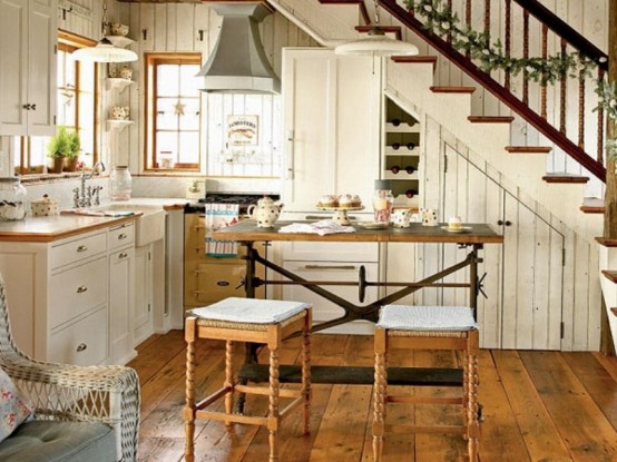 a small farmhouse kitchen with white cabinets, light-stained countertops, a vintage table and carved stools, and hanging lamps