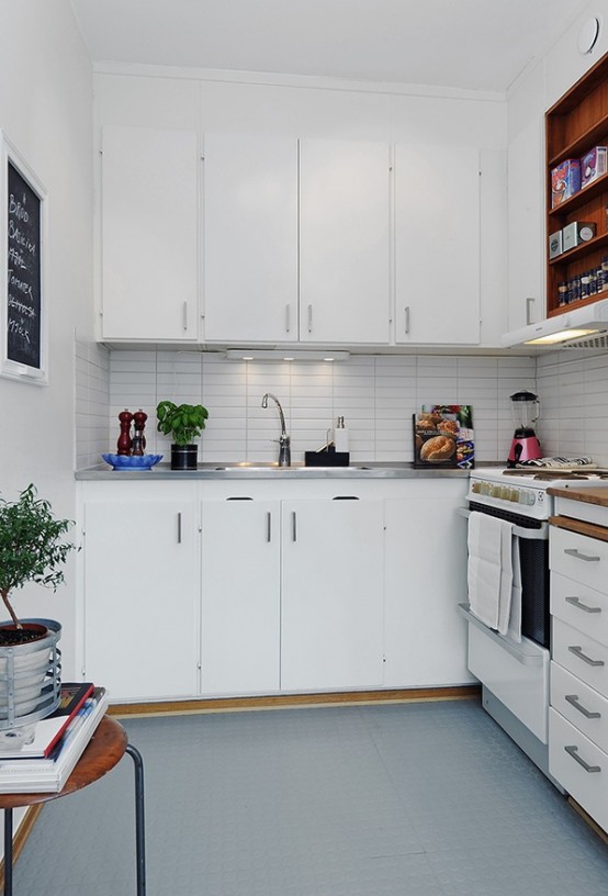 A small, minimalist kitchen in white with a tiled splashback, lighting and a stool for storage