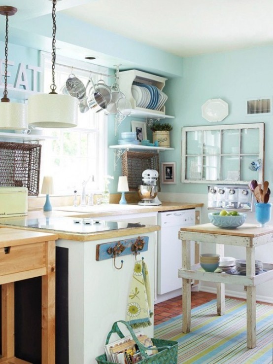 a small, vintage-style aqua kitchen with neutral cabinets and light-stained countertops, a small island, open shelving, and pendant lamps
