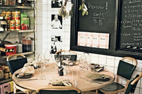 a small industrial mela room with a round wooden table, leather chairs, open shelves and chalkboards
