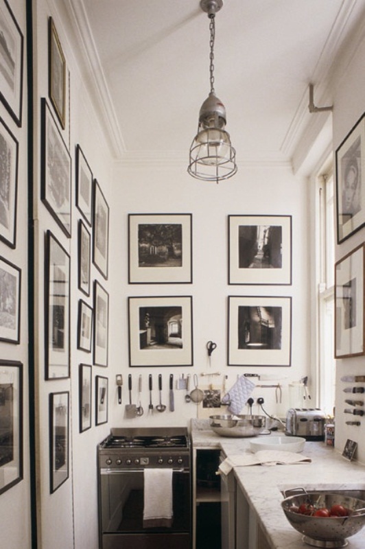 a small, monochromatic kitchen with neutral cabinets and countertops, black-and-white photos on the walls, and a pendant lamp