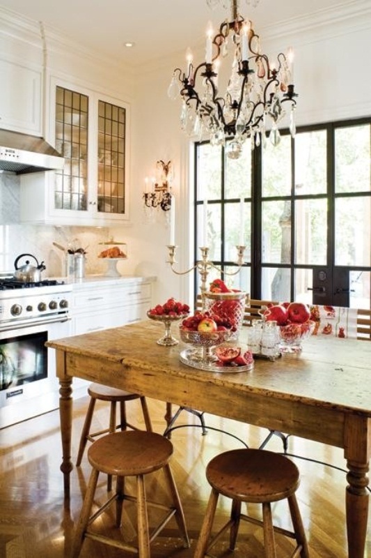 a small, eclectic kitchen with white farmhouse cabinets, a vintage wooden dining set, and a large crystal chandelier