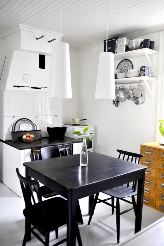 a small, eclectic kitchen with a white cabinet, a black countertop, white pendant lamps, a black vintage dining set and an apothecary cabinet