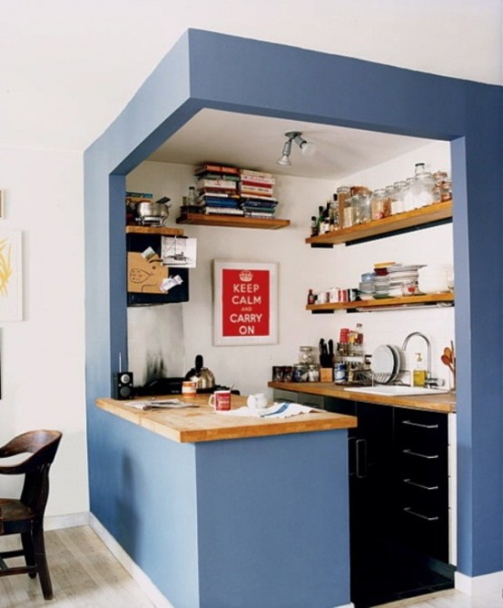 a small kitchen in a blue cube with black built-in cupboards, light wood worktops and open shelves