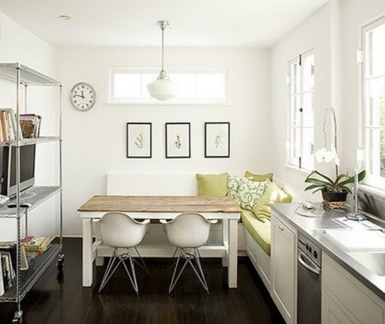 a small modern kitchen in white with an L-shaped bench, a wooden table and a large open storage space