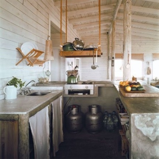 A small rustic industrial kitchen with concrete countertops, metal pots and hanging wooden shelves