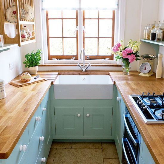 a small pastel farmhouse kitchen with mint cabinets, butcher block countertops, open wood shelving, and a wood-framed window