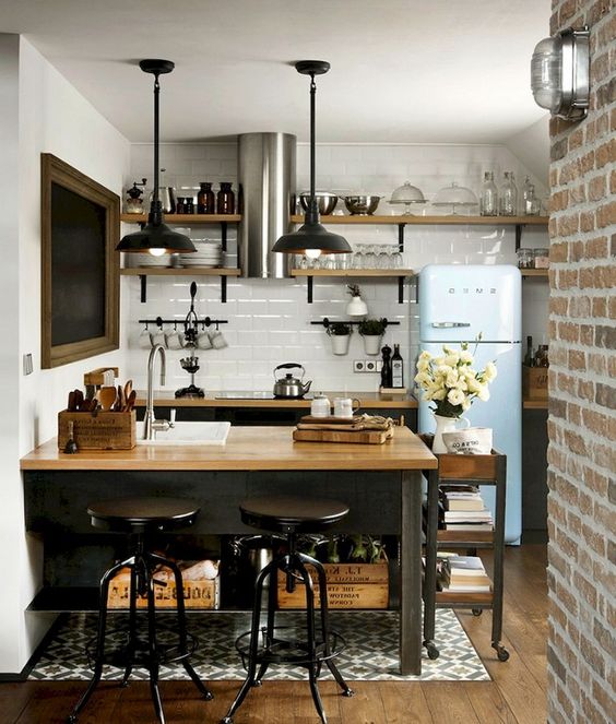 a small industrial kitchen with black cabinets and an island, as well as butcher block countertops, black pendant lights and a blue refrigerator